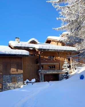 Una cabaña de madera con base de piedra, varios balcones y un techo cubierto de nieve.