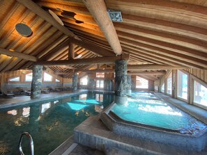 Una piscina interior con pilares de piedra, vigas de madera y agua cristalina.