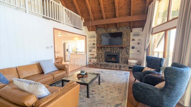 A spacious living room with a high ceiling, a stone fireplace, a large window, and a balcony. - Quiet, Overlook Golf Course, Close to Town, Shopping and Dining (Pagosa Springs)