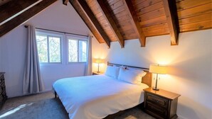 A bedroom with a sloped ceiling, a large bed with white bedding, two bedside lamps, and a window with curtains.