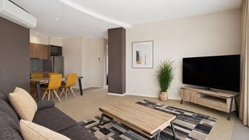 A modern living room with a sofa, a coffee table, a TV, and a dining area with chairs.