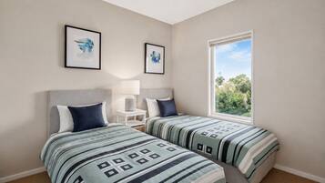 A bedroom with two beds, a window with a view, and two framed pictures on the wall.