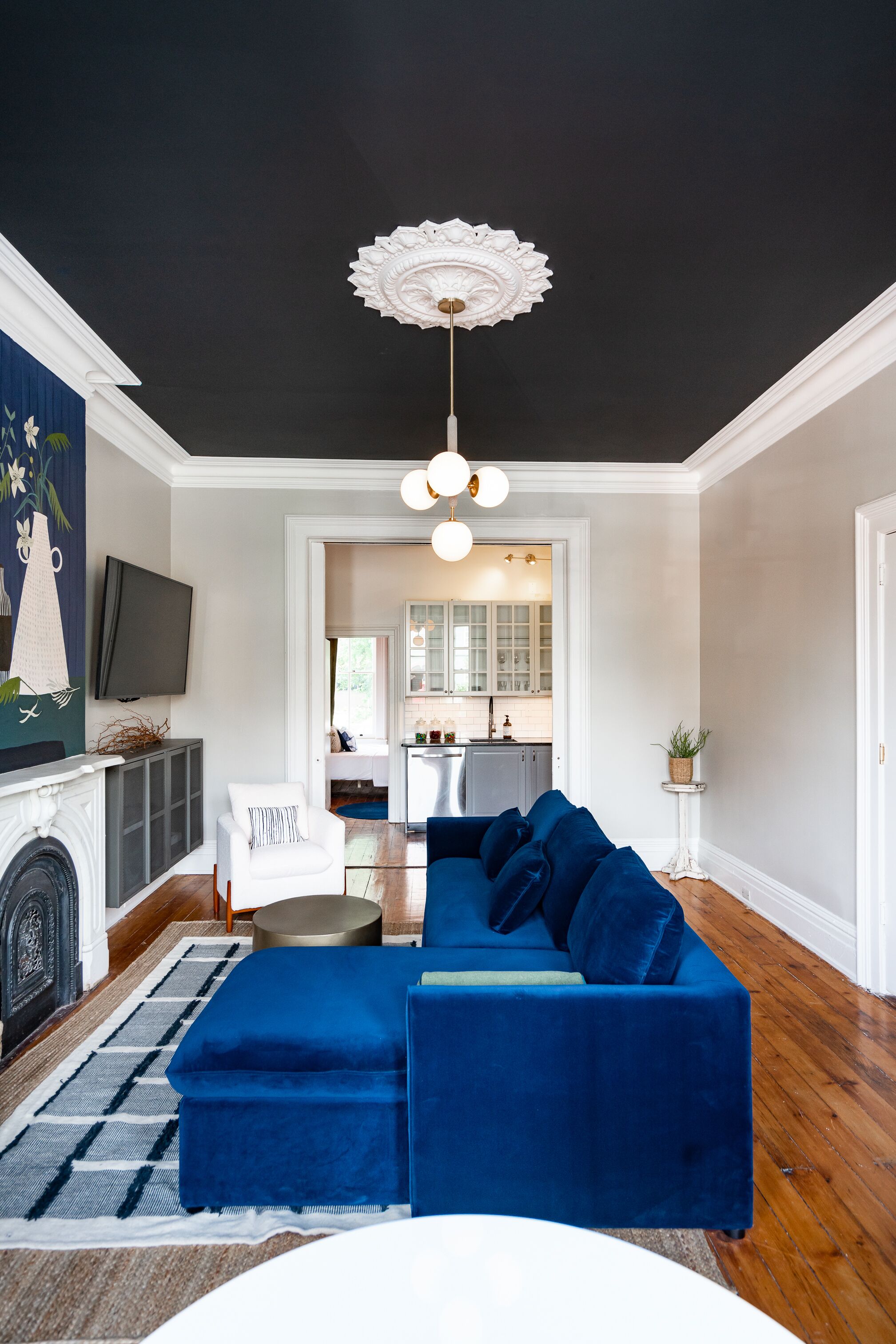 A living room with a dark ceiling, a blue sectional sofa, a white armchair, and a fireplace.