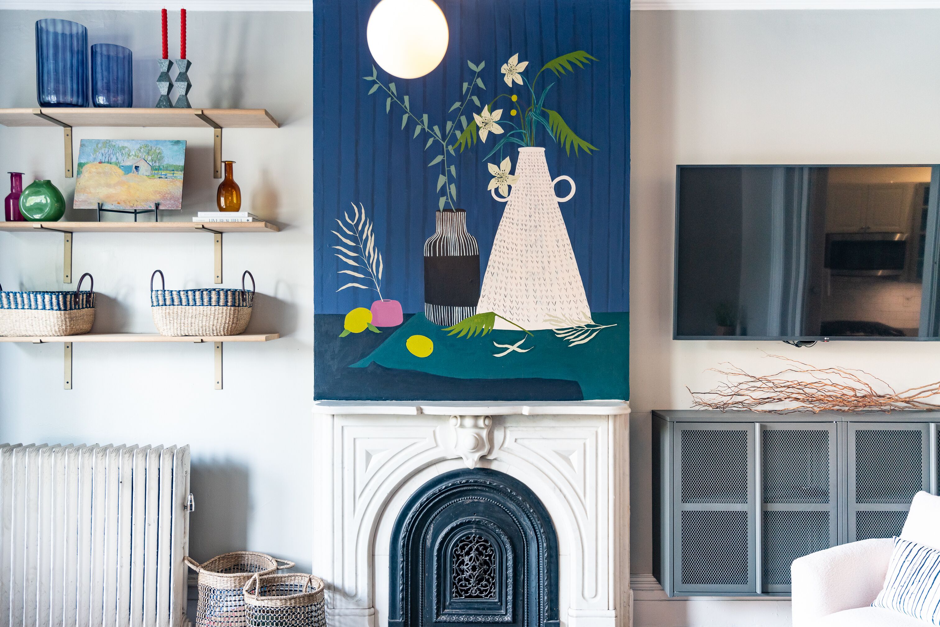 Un salon avec une cheminée, un tableau au-dessus et des étagères remplies de divers objets.