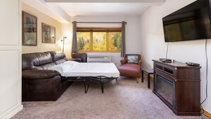 A cozy room with a sofa, a flat-screen TV, a fireplace, and a window with autumn foliage. - 5087 Gateway Home by RedAwning (Keystone)