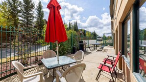 A patio with a table and chairs, a red umbrella, and a view of trees and a road. - 5087 Gateway Home by RedAwning (Keystone)