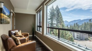 A room with a large window offering a mountain view, a brown leather chair, and a small plant. - DELUXE SLOPESIDE Condo with 4th FLOOR VIEWS, Elevator and Underground Parking at Canyon Lodge (1849 Condos 409) by RedAwning (Mammoth Lakes)
