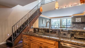 A kitchen with a granite countertop, stainless steel appliances, wooden cabinets, and a staircase with a metal railing. - DELUXE SLOPESIDE Condo with 4th FLOOR VIEWS, Elevator and Underground Parking at Canyon Lodge (1849 Condos 409) by RedAwning (Mammoth Lakes)