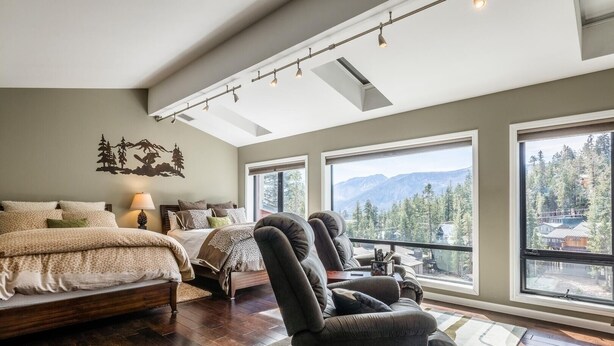 A spacious bedroom with a large bed, two armchairs, and a view of mountains through large windows. - DELUXE SLOPESIDE Condo with 4th FLOOR VIEWS, Elevator and Underground Parking at Canyon Lodge (1849 Condos 409) by RedAwning (Mammoth Lakes)