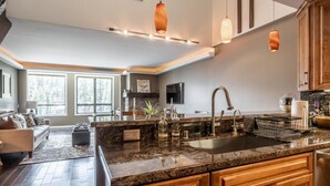 A modern kitchen with granite countertops, wooden cabinets, and pendant lighting. - DELUXE SLOPESIDE Condo with 4th FLOOR VIEWS, Elevator and Underground Parking at Canyon Lodge (1849 Condos 409) by RedAwning (Mammoth Lakes)
