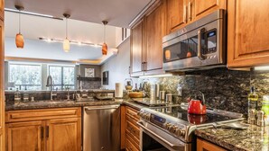 A modern kitchen with wooden cabinets, stainless steel appliances, granite countertops, and pendant lighting. - DELUXE SLOPESIDE Condo with 4th FLOOR VIEWS, Elevator and Underground Parking at Canyon Lodge (1849 Condos 409) by RedAwning (Mammoth Lakes)