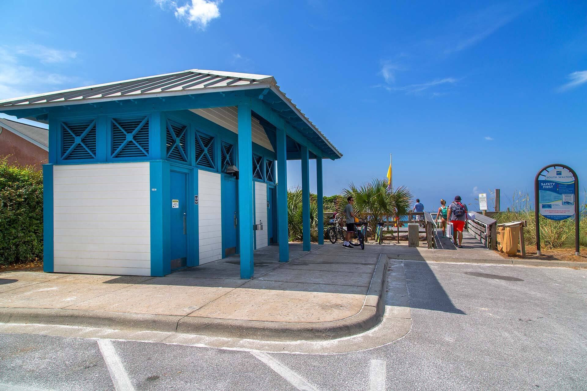 A covered outdoor area with a blue and white building, a signboard, and a pathway leading to a beach.