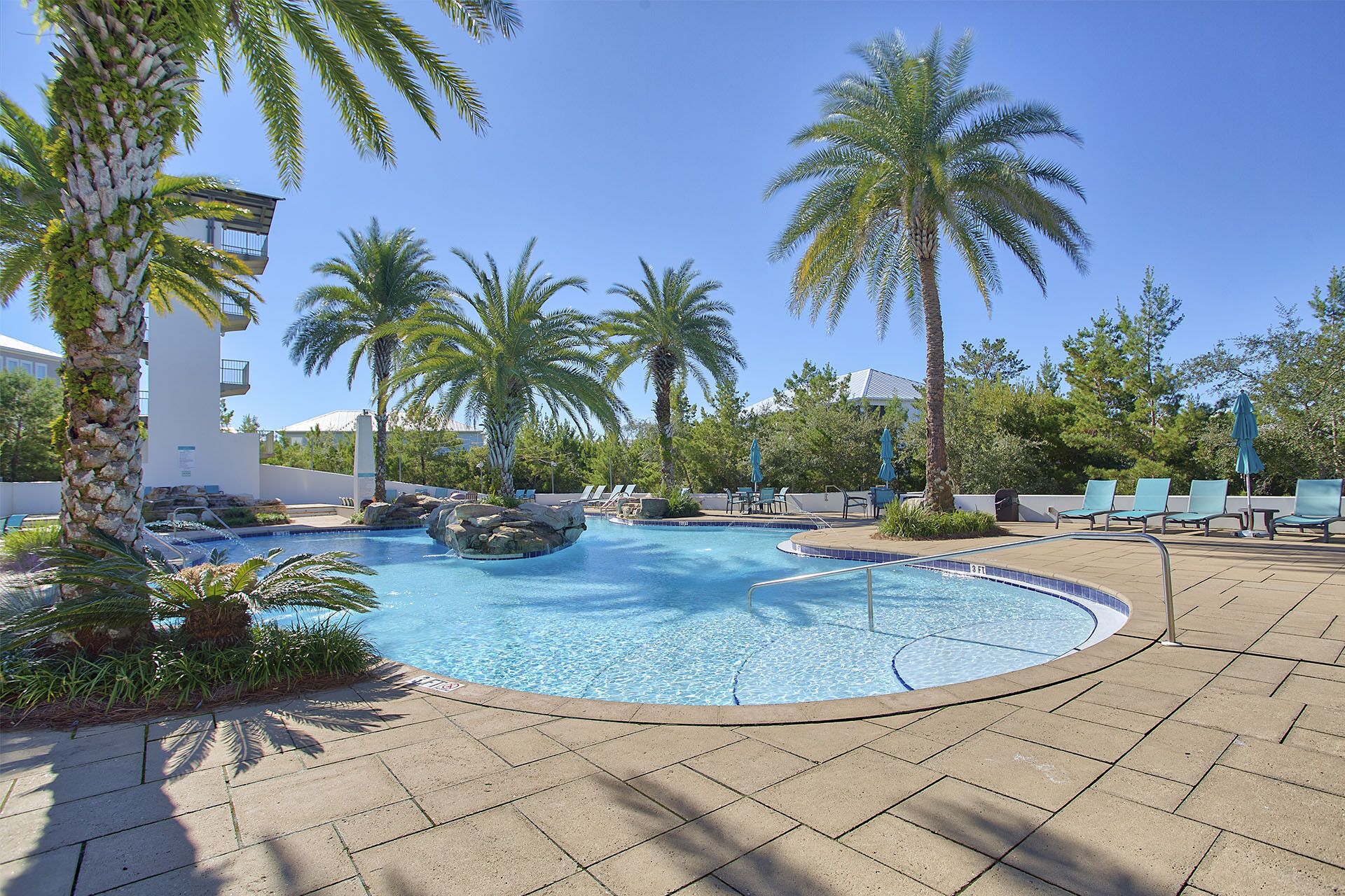 A pool area with palm trees, lounge chairs, and a clear blue sky.