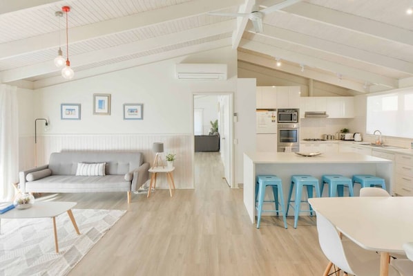 Une cuisine moderne avec des meubles blancs, un îlot central doté de tabourets et un coin repas avec une table et des chaises blanches.