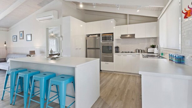A modern kitchen with white cabinetry, a central island with bar stools, stainless steel appliances, and a bright, airy ceiling design. - Seaesta Rye by Ready Set Stay - Pet-friendly, solar heated pool, WIFI, Netflix (Rye)