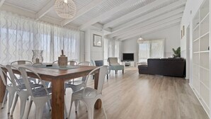 A spacious living area with a wooden dining table, white chairs, and a dark-colored sofa. - Seaesta Rye by Ready Set Stay - Pet-friendly, solar heated pool, WIFI, Netflix (Rye)