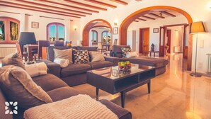 Amplia sala de estar con un sofá seccional grande, una mesa de centro y una chimenea. Hay varias zonas de estar y vistas al exterior.
