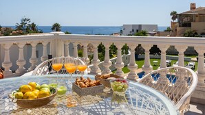 Een tafel gedekt met fruit, croissants en sinaasappelsap op een balkon met uitzicht op zee.