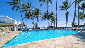 A swimming pool with stone flooring, surrounded by palm trees and lounge chairs.