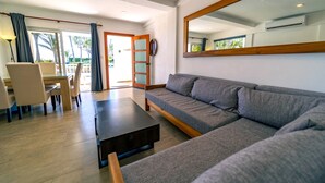 A modern living room with a grey sofa, wooden coffee table, and a dining area with chairs and a table.