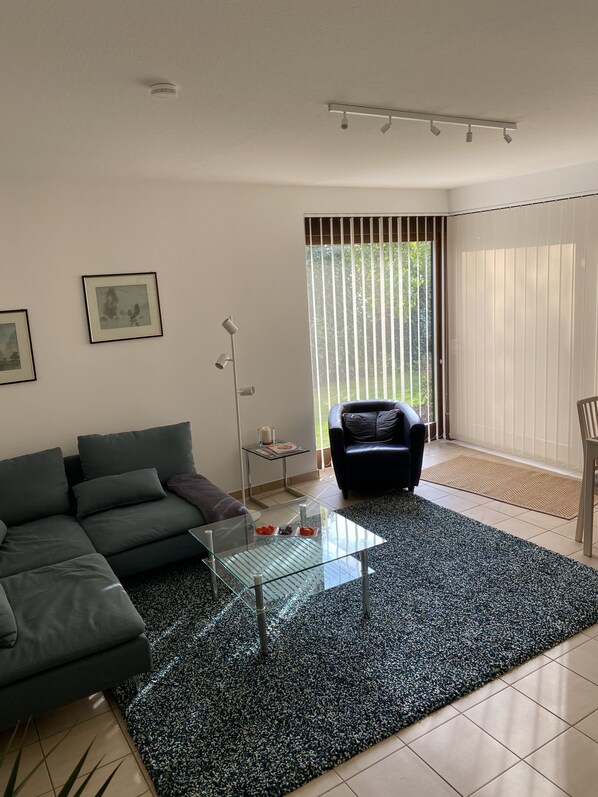 A modern living room with a sectional sofa, a glass coffee table, and a large window with blinds.