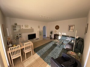 Un salon moderne comprenant un téléviseur, un canapé, une table à manger, des chaises et un tapis à motifs.