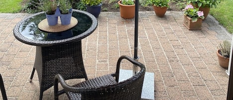 A patio with a round table and chairs, surrounded by potted plants and a red umbrella.