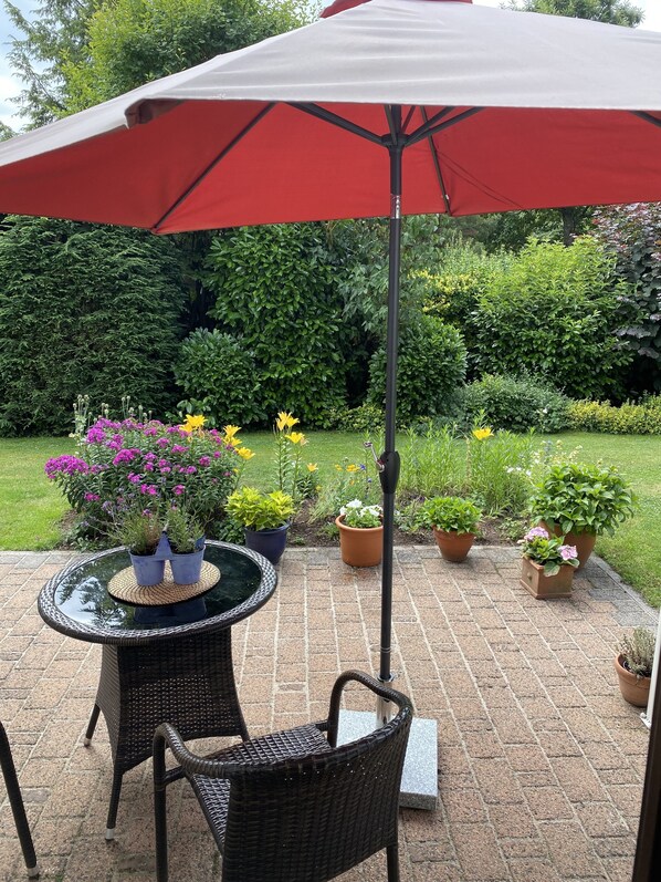 A patio with a round table and chairs, surrounded by potted plants and a red umbrella.
