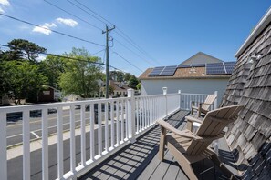 Una terraza con sillas, barandal blanco y una casa con paneles solares.