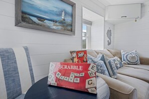 Una caja del juego Scrabble sobre una mesa en una habitación con un cuadro de un faro, un sofá y un adorno de pared.