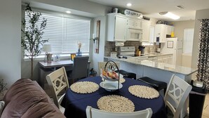 A dining area with a table set for four, surrounded by chairs. A kitchen with white cabinets and a countertop is visible in the background. - Walk-In Unit W/Lake View and Close to SDC (Branson)