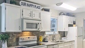 A modern kitchen with white cabinets, a granite countertop, a microwave, and a sign that reads "OUR HAPPY PLACE". - Walk-In Unit W/Lake View and Close to SDC (Branson)