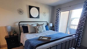 A bedroom with a bed, a nightstand, a lamp, and a window with curtains. - Walk-In Unit W/Lake View and Close to SDC (Branson)