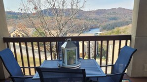 A balcony with a table and chairs, a lantern, and a view of a river and hills. - Walk-In Unit W/Lake View and Close to SDC (Branson)