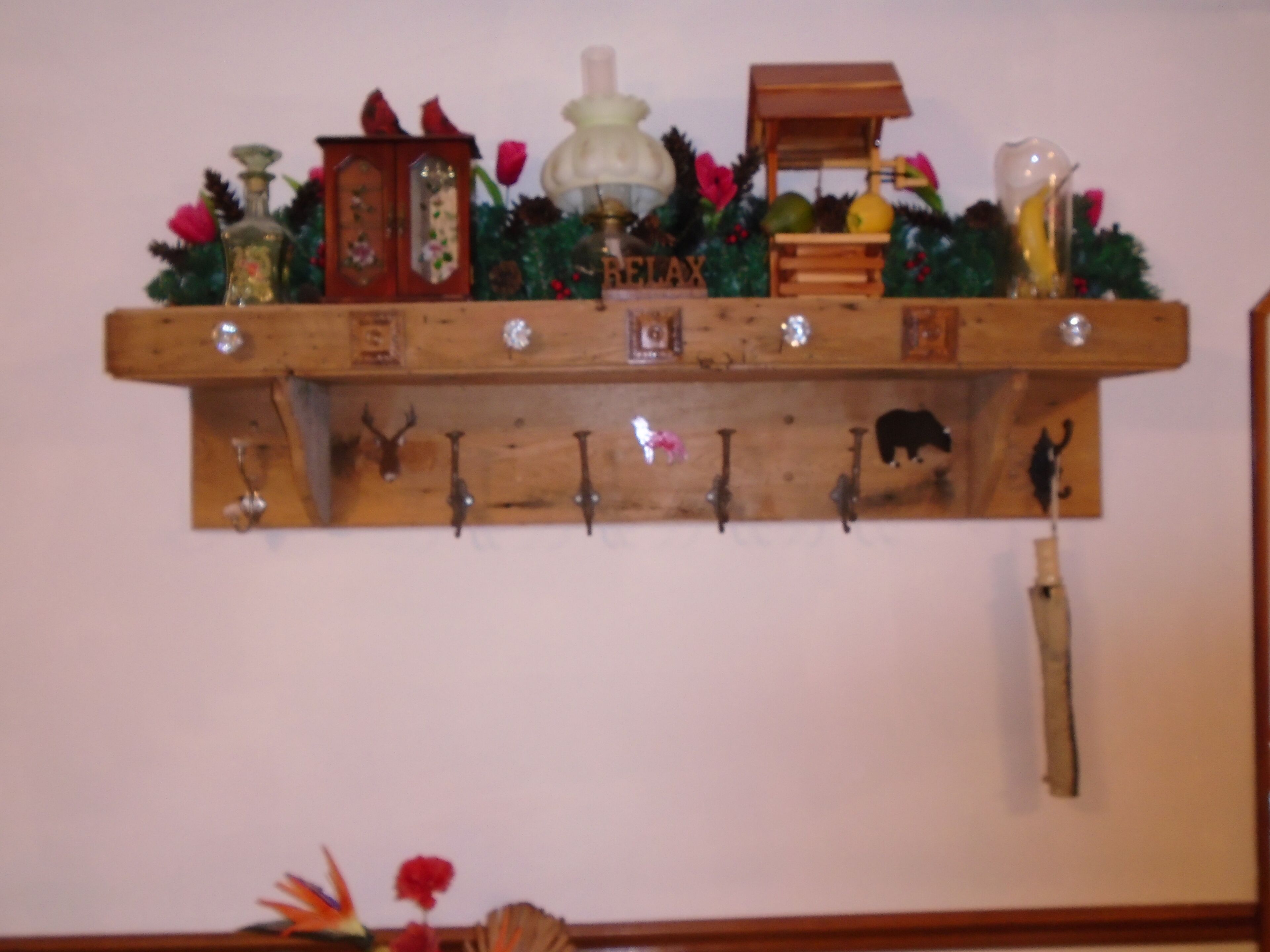 A wooden shelf with various decorative items, including a clock, a lamp, and a small wooden structure.