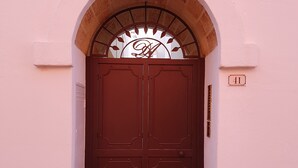 A double door with an arched entrance, a decorative metal sign above, and a number plaque on the wall. - Dimora di charme "Corte della Torre" - Morciano di Leuca - Italy (Morciano di Leuca)