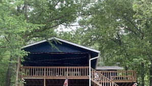 Une cabane en bois à deux étages, dotée d’une terrasse, d’un drapeau américain et d’un quai menant à un petit bateau.