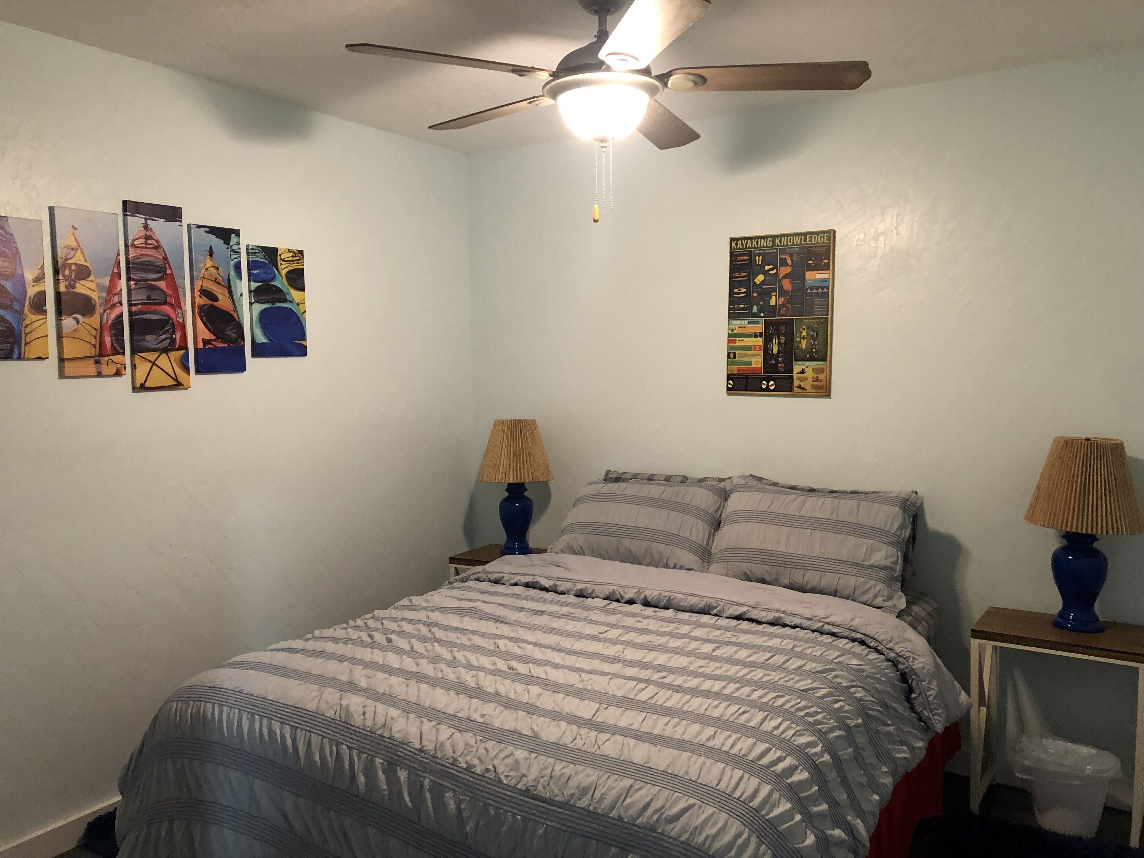 A bedroom with a bed, two bedside tables with lamps, a ceiling fan, and wall art.