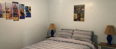 A bedroom with a bed, two bedside tables with lamps, a ceiling fan, and wall art.
