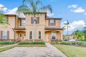 Un edificio residenziale di due piani con facciata beige, un ingresso centrale con il numero 241 e un giardino anteriore curato con un vialetto che conduce all'ingresso.