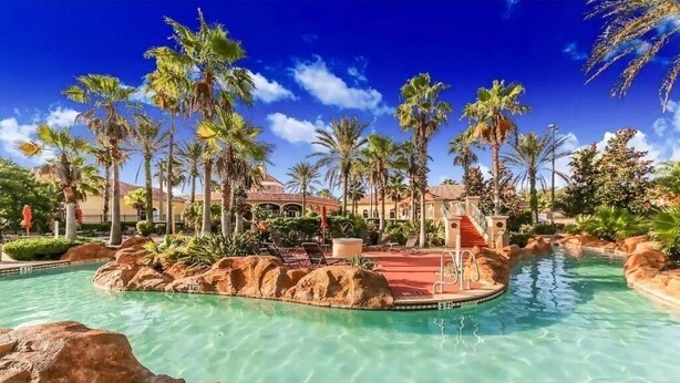Zona de piscina en un resort con agua cristalina, palmeras y un edificio al fondo.