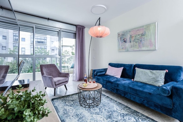 A modern living room with a blue sofa, a round coffee table, and a large window with curtains.
