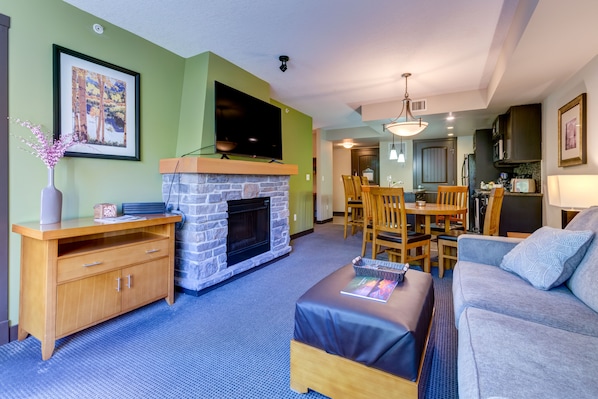 A living room with a stone fireplace, a flat-screen TV, a wooden coffee table, and a grey sofa.