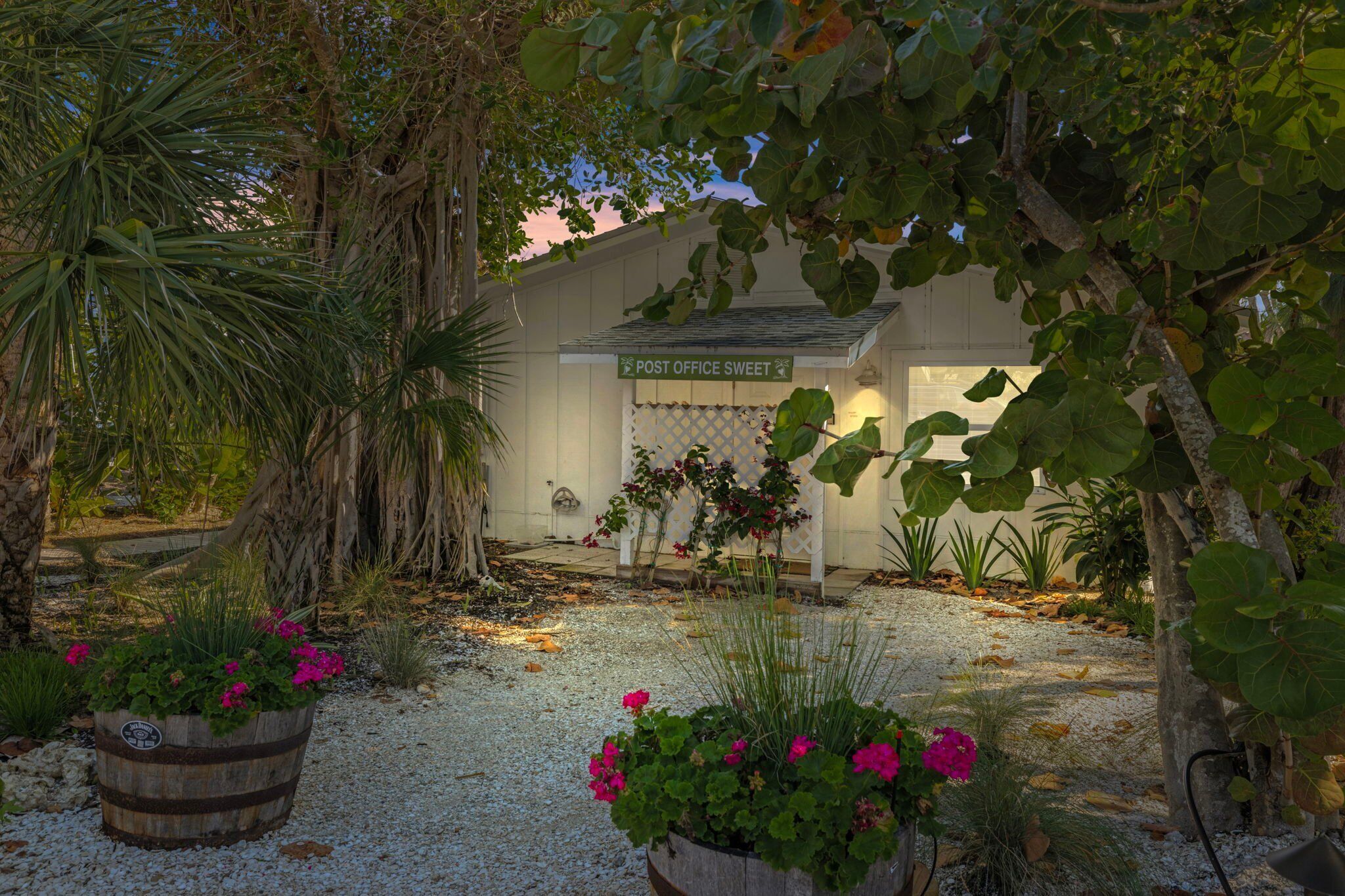 A post office with a sign reading "POST OFFICE SWEET" surrounded by lush greenery and flowering plants.