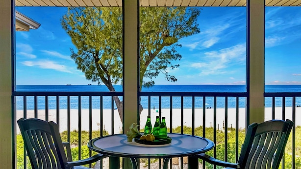 A covered outdoor seating area with a table and chairs, overlooking a beach. - Breathtaking Views - Romantic Honeymoon Suite - Jensen's "On the Gulf" 4 (Captiva)