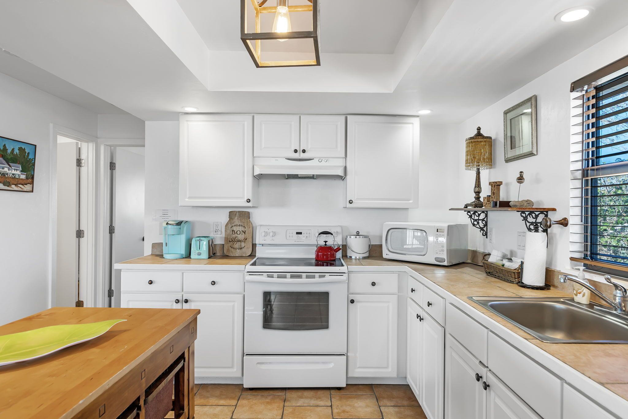 Une cuisine moderne avec des meubles blancs, une table en bois, une cuisinière, un four à micro-ondes et un évier.