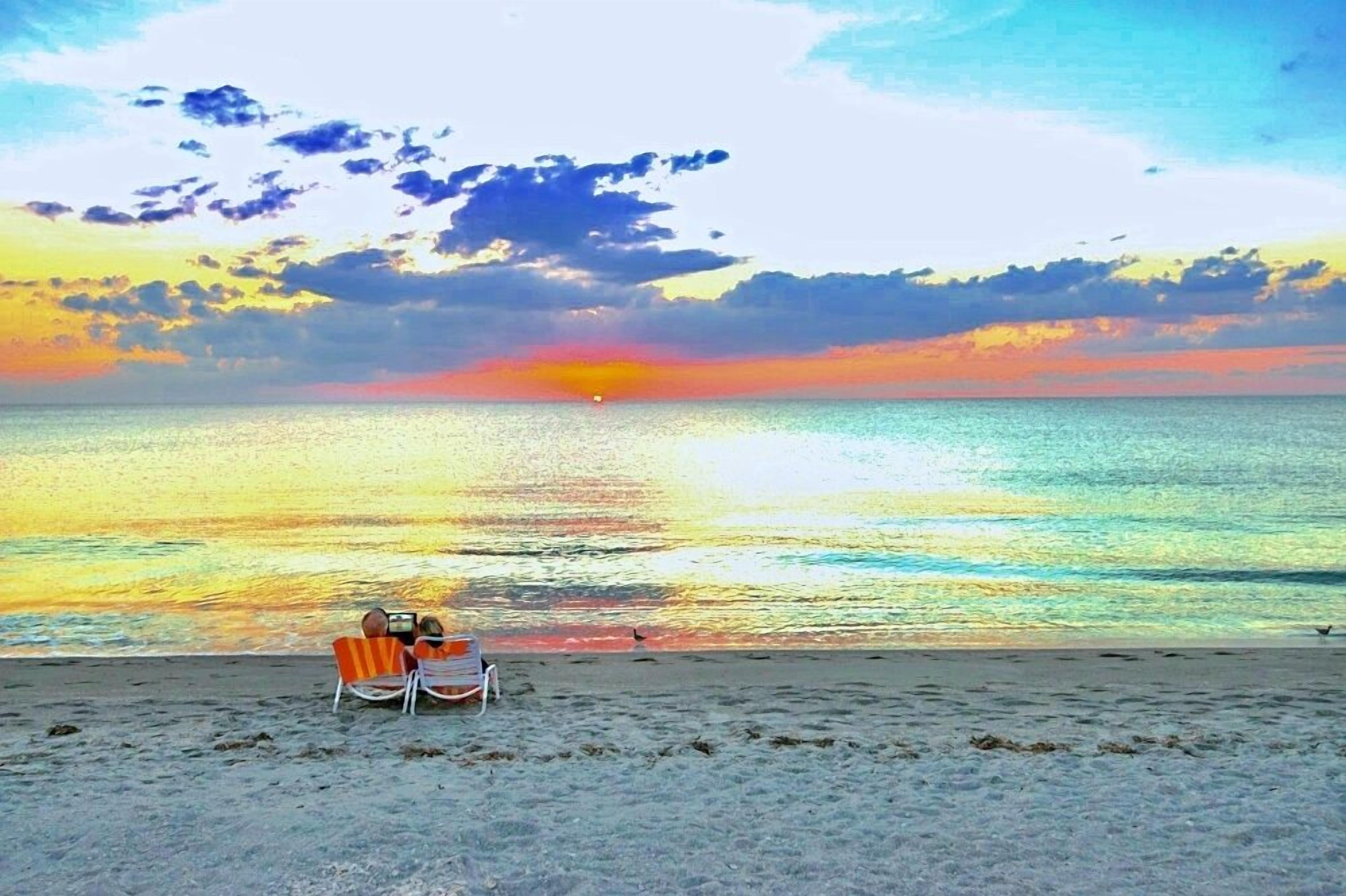 Ein Strand mit zwei Stühlen, die auf den Sonnenuntergang über dem Meer ausgerichtet sind.