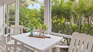 Una mesa blanca con sillas en una terraza de madera, con vistas a un follaje exuberante y palmeras.