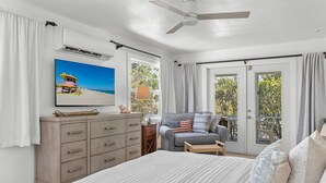 Une chambre à coucher comprenant un lit, une commode, un téléviseur, un ventilateur de plafond et une porte-fenêtre coulissante donnant sur un balcon.