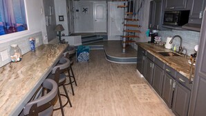 A kitchen with a marble countertop, wooden stools, a microwave, and a staircase. - Beach Vibes (Spring Valley)